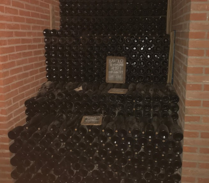 Hundreds of bottles of Barolo Tettimorra Scarpa stacked in a stair-like pattern in a brick cellar.